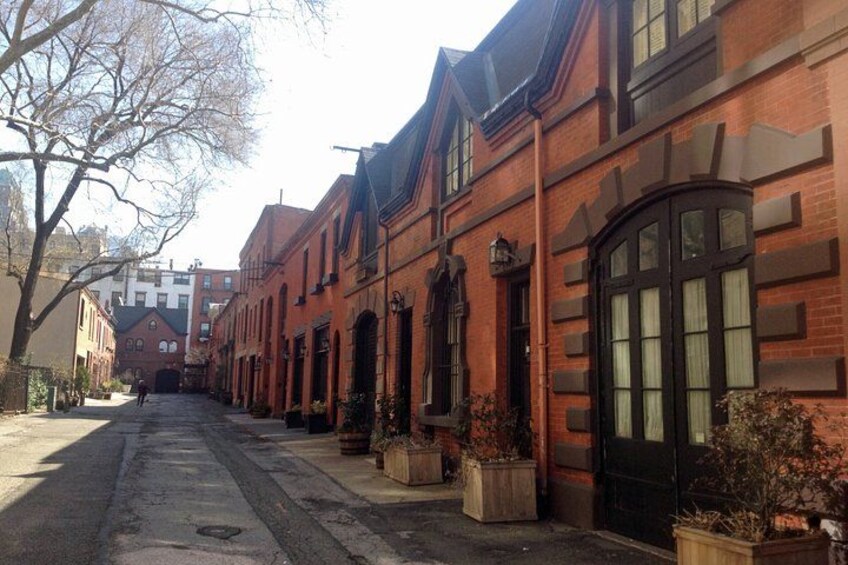 A quiet street lined with brick buildings, a tree, and potted plants. 1