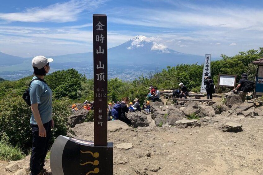 A mountain peak with a sign, a person standing, and a view of a snow-capped mountain in the background. 3
