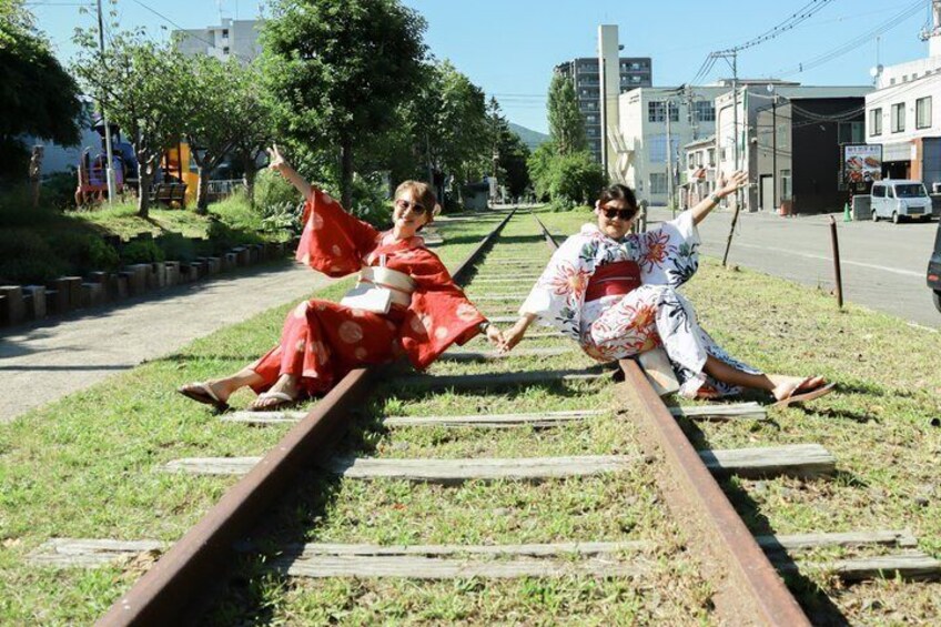 Two individuals sitting on railway tracks in a park, dressed in traditional Japanese attire. 3