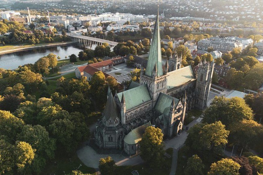A historic church with a tall spire, surrounded by trees and a river. 1