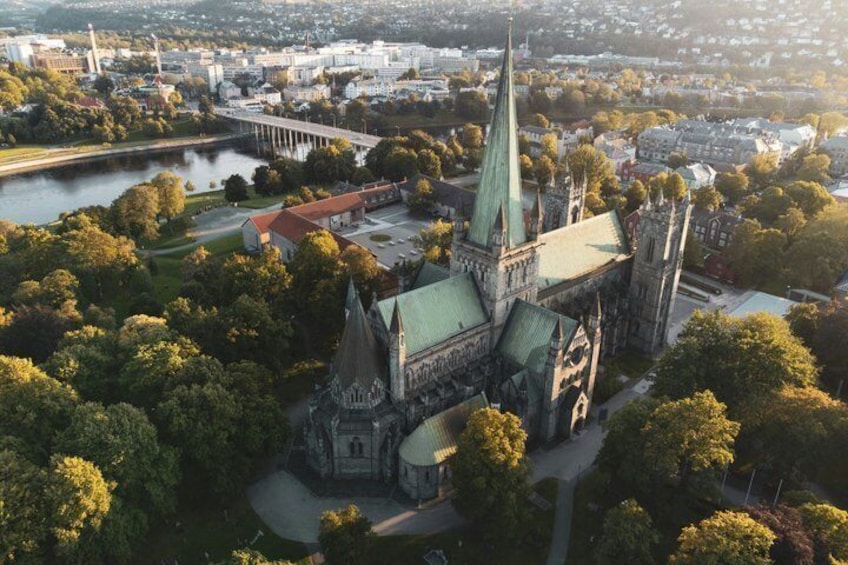 An aerial view of a historic church with a tall spire, surrounded by trees and a river. 1