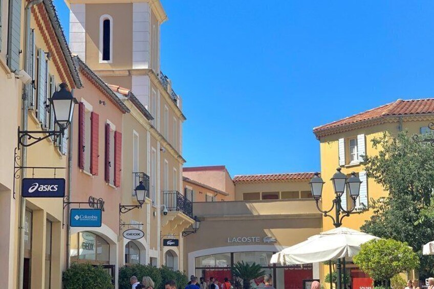 A street with buildings, a Lacoste sign, and outdoor seating. 2