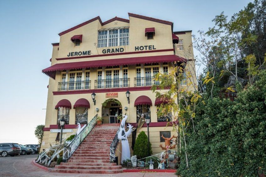The Jerome Grand Hotel with a red and beige facade, a central entrance, and a staircase leading up to the main entrance. 1