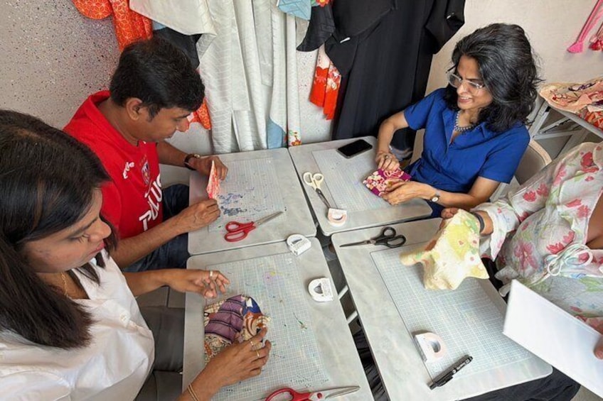 A group of people engaged in a crafting activity at a table with scissors, fabric, and a mobile phone. 2