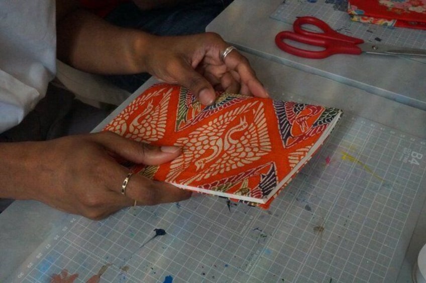 Hands holding a patterned book on a cutting mat with scissors and fabric pieces. 3