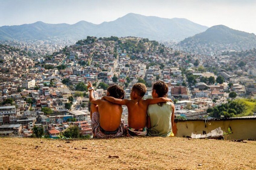 Two people sitting on a hill overlooking a densely populated city with mountains in the background. 2