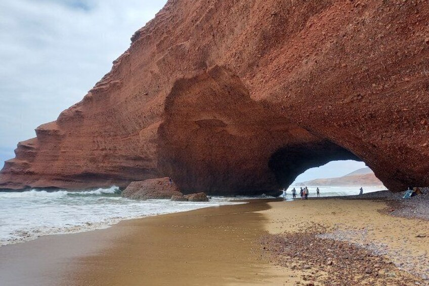 A large red rock formation with a natural arch over a beach. 1