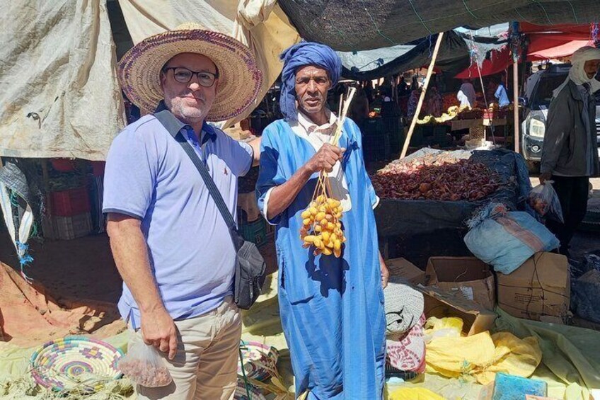 Two people at a market stall with goods and a tent in the background. 4