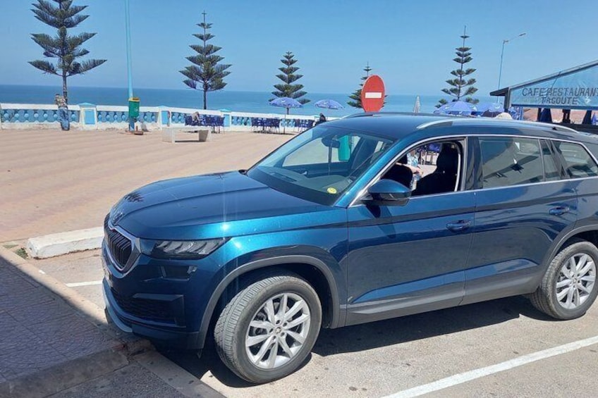 A blue SUV parked on a beachside road with a view of the ocean and palm trees in the background. 3