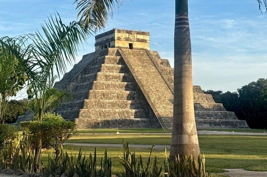 A large pyramid structure with a stepped design, surrounded by a grassy area and palm trees. 5