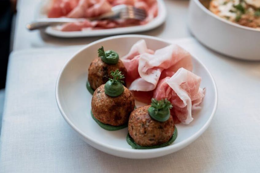 A plate with meatballs and prosciutto on a white tablecloth. 5