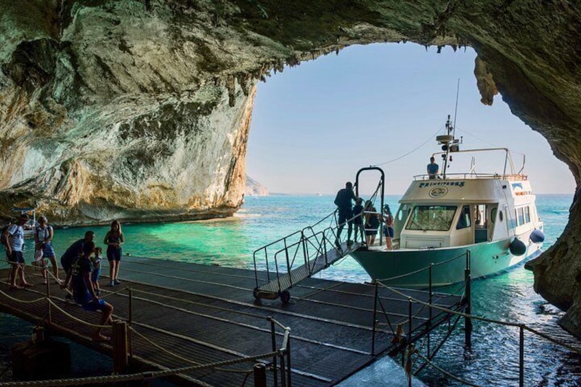 A boat docked at a cave opening with people on a nearby pier. 1