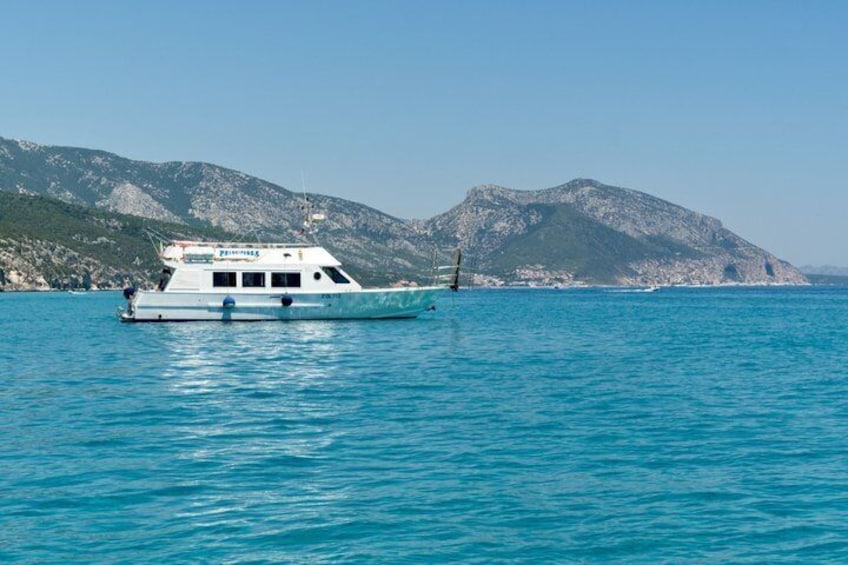 A boat on calm blue water with a mountainous coastline in the background. 4
