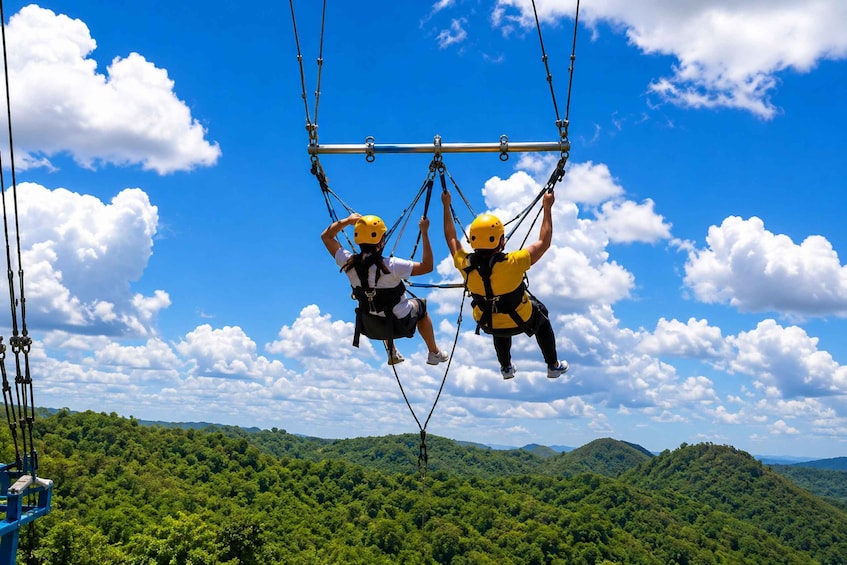 Two people bungee jumping with safety harnesses, with a clear blue sky and a forested landscape below. 5