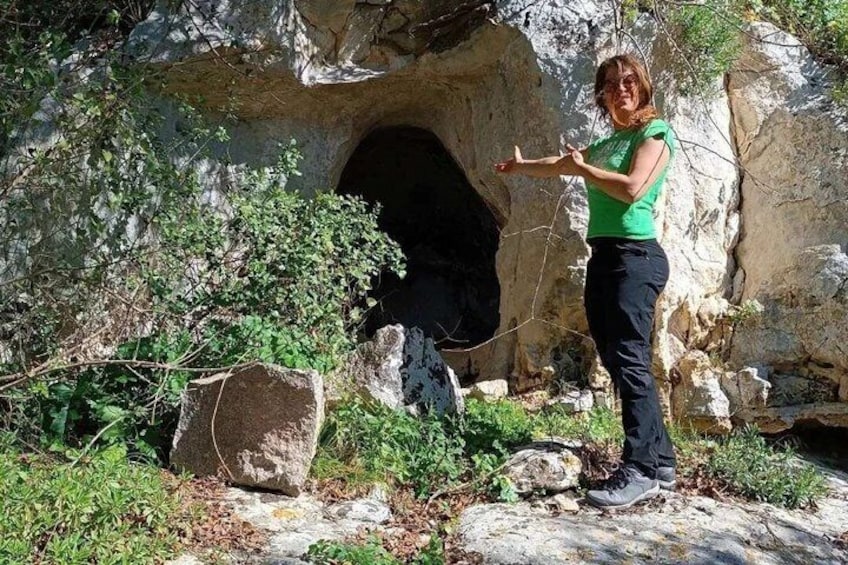A person standing in front of a cave entrance with vegetation around. 1