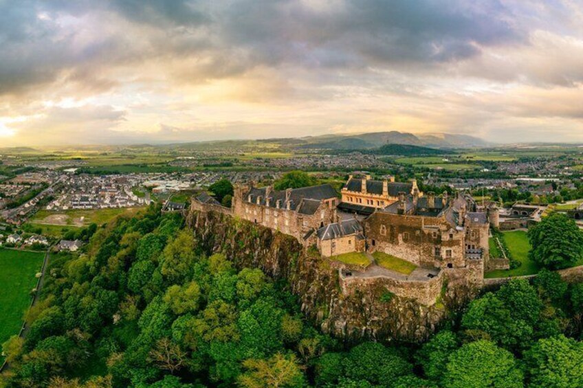A historic castle on a hill overlooking a town, surrounded by lush greenery. 1