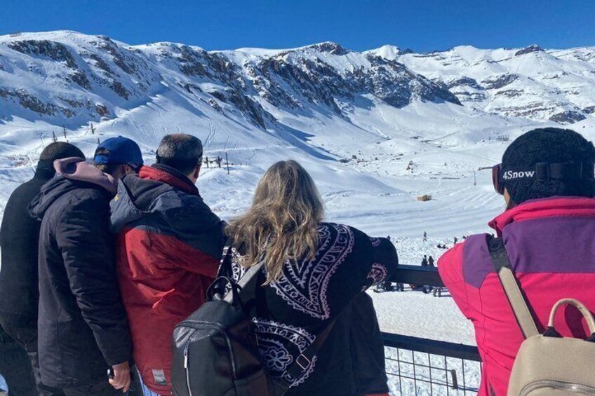 A group of people standing on a snowy mountain slope, overlooking a ski slope. 3