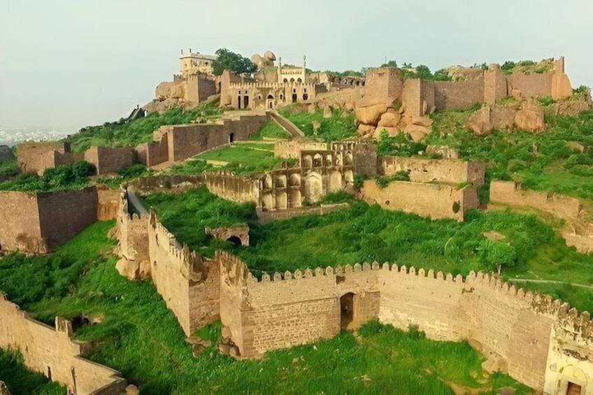 A historic fort with walls and towers, surrounded by lush greenery. 1