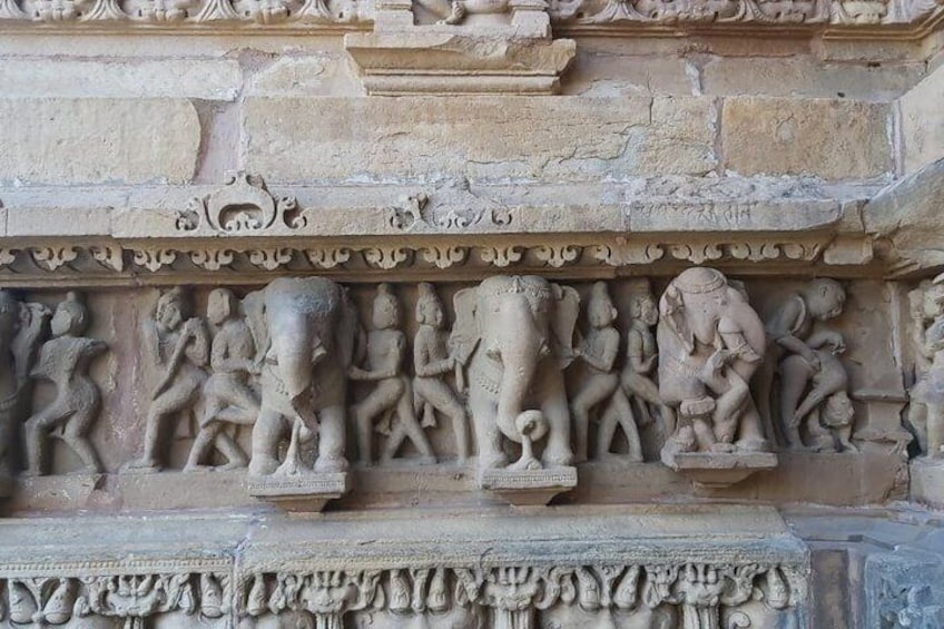 A detailed stone carving of a procession with elephants and figures, set in a temple or historical structure. 5