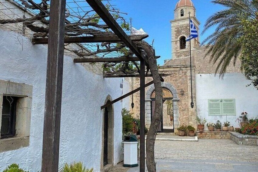 A courtyard with a white building, a pergola, a stone tower, and a flag. 2