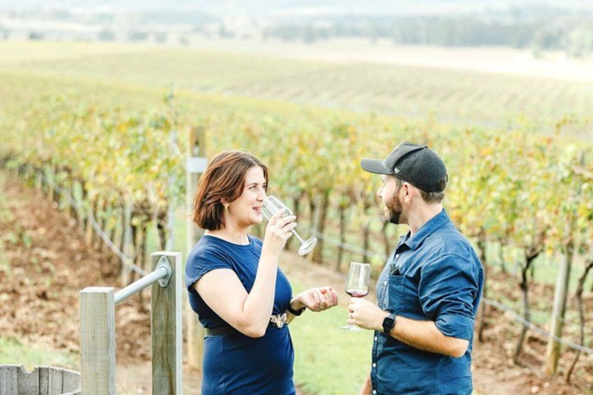 Two people in a vineyard holding glasses, likely tasting wine. 3