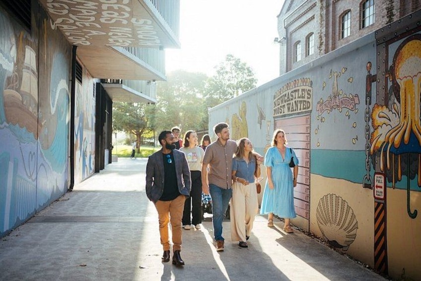 A group of people walking on a sidewalk next to a building with colorful murals. 4