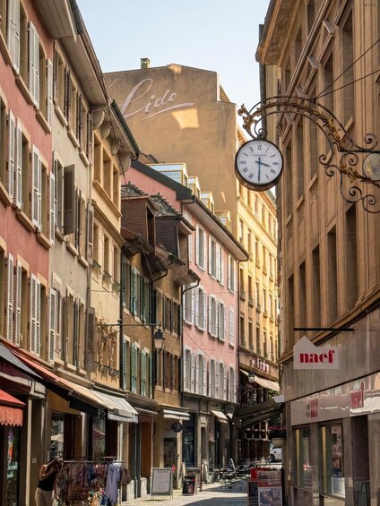 A narrow street lined with colorful buildings, a large clock, and various storefronts. 5