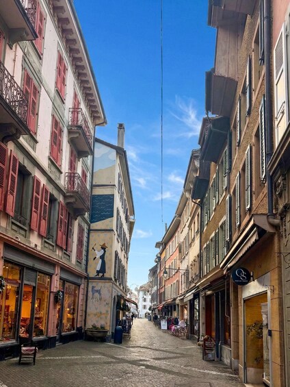 A cobblestone street lined with historic buildings, some with balconies and shutters, under a clear blue sky. 3