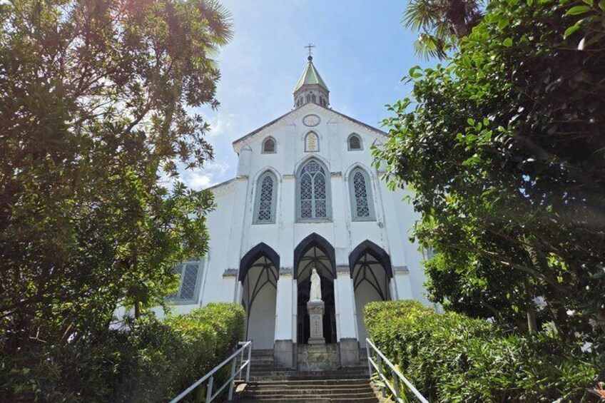 A white church with a steeple, surrounded by greenery and a staircase leading up to the entrance. 4