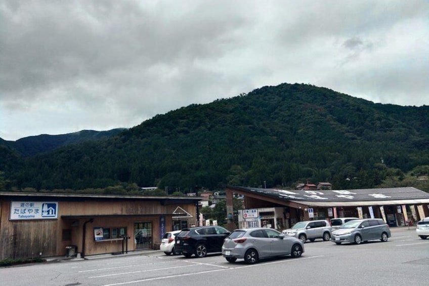 A parking lot with several cars, a building with a sign, and a forested hill in the background. 2