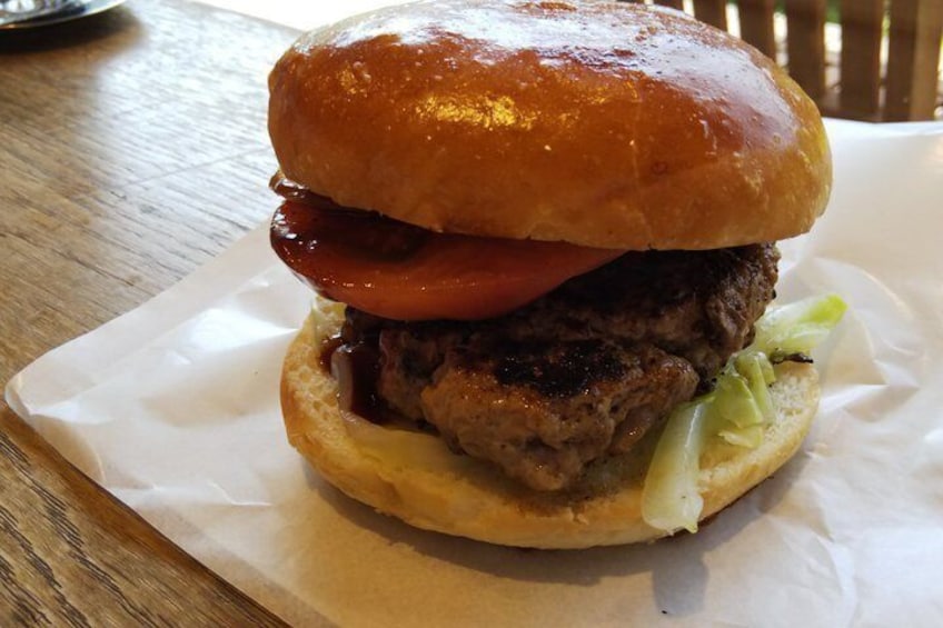 A burger with a sesame seed bun, lettuce, tomato, and a beef patty, served on a white paper plate. 4