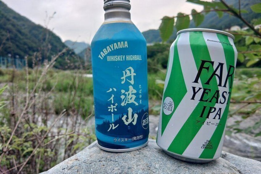 A bottle of Tabayama whiskey highball and a can of Far Yeast IPA beer on a stone surface with a mountainous landscape in the background. 5