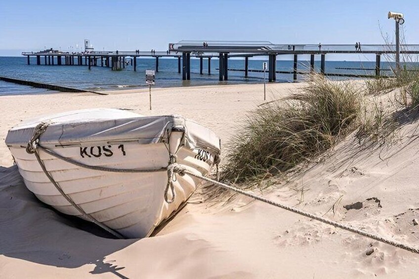 A boat named KOS 1 tied to a sandbank near a pier. 3