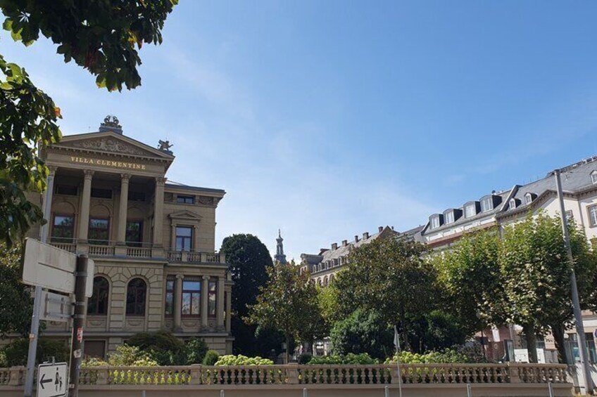 Villa Clementine, a classical building with columns and a balcony, surrounded by trees and other historic architecture. 5