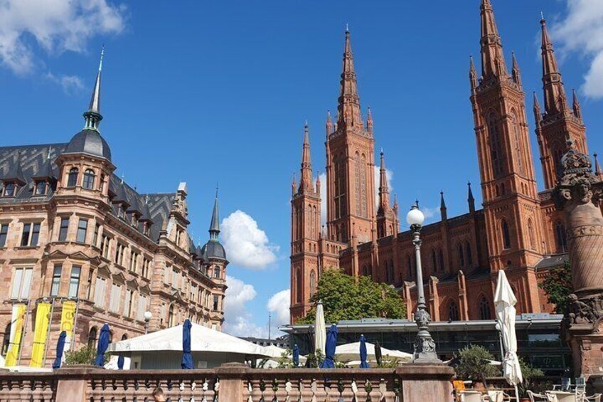 A historic building with multiple spires and a large dome, surrounded by trees and a clear sky. 1