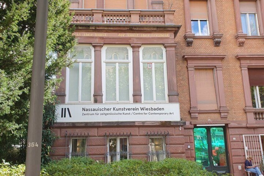 A building with a sign reading 'Nassauischer Kunstverein Wiesbaden' and a large window. 5