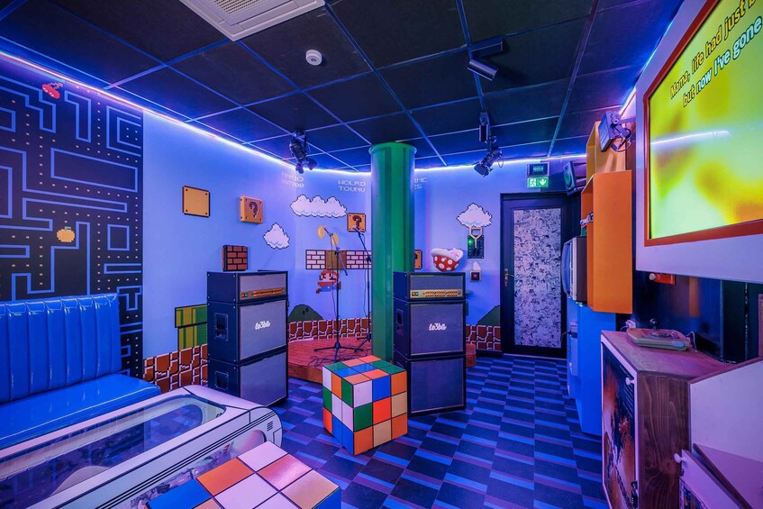 A room with a checkered floor, a large Rubik's cube, and a projection screen with text. 2