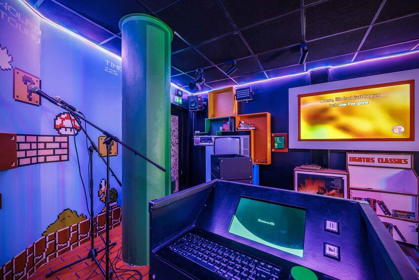 A retro-themed room with a large green pillar, a computer setup, and a wall with pixel art and a screen displaying a quote. 5