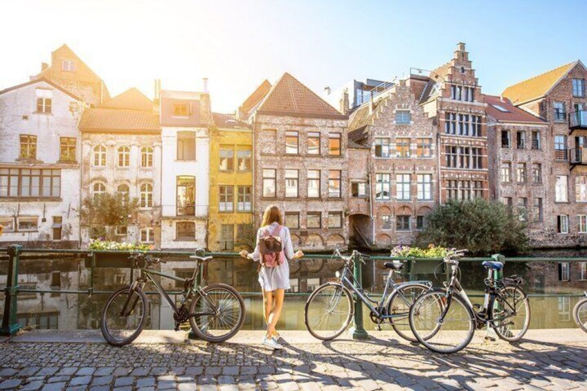A person standing by a canal with bicycles, historic buildings, and a bridge in the background. 3