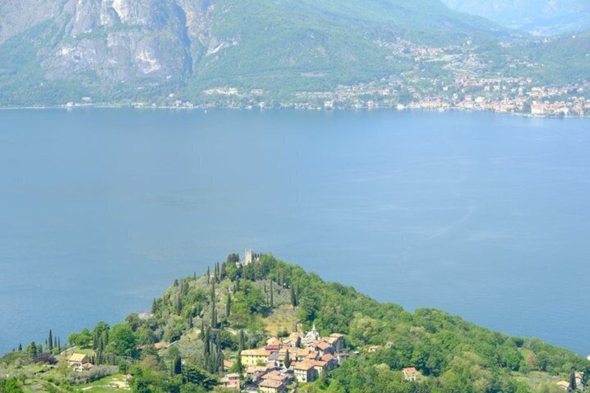 A lake surrounded by mountains, a small island with buildings, and a distant town. 2