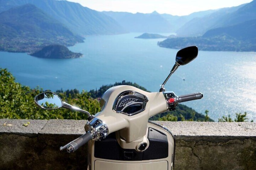 A scooter parked on a ledge overlooking a lake with mountains in the background. 1