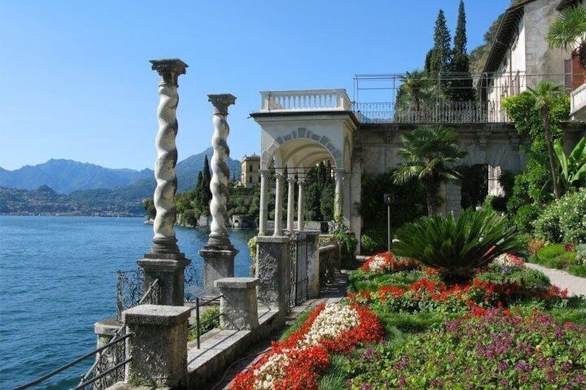 A waterfront garden with stone balustrades, a fountain, and colorful flowers. 5