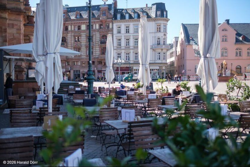 Outdoor cafe seating with umbrellas, a cobblestone street, and historic buildings in the background. 3