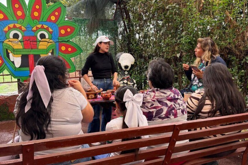 A group of people sitting on a bench outdoors, engaged in a meal with a colorful mural in the background. 4