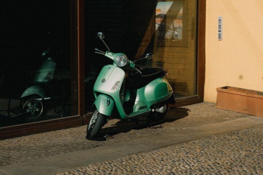 A green scooter parked in front of a building with a window and a door. 3