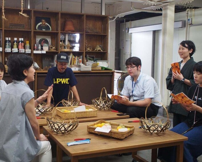 A group of people in a room with wooden shelves, baskets, and a table with items on it. 1
