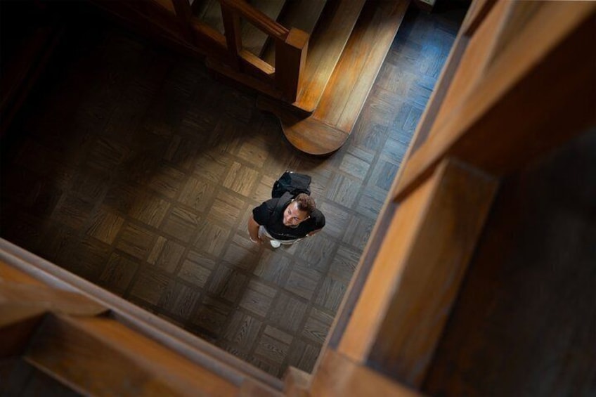 A person standing on a wooden floor with a backpack, surrounded by wooden beams and a staircase. 4