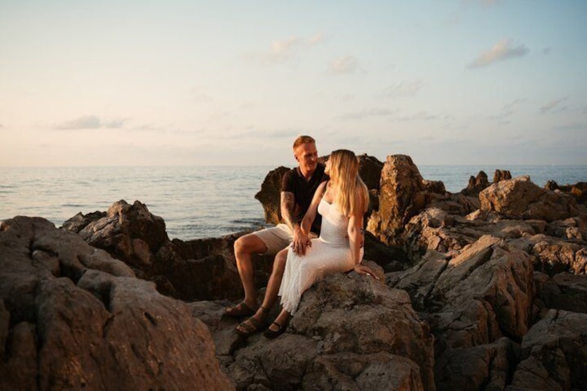 A couple sitting on rocky terrain by the sea during sunset. 3