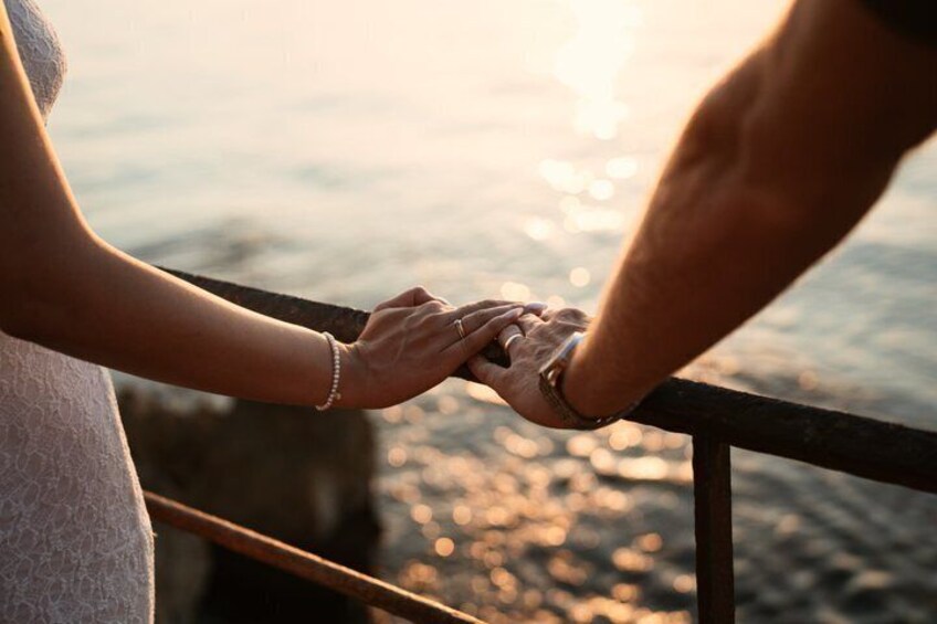 A couple holding hands by a railing with a sunset in the background. 2