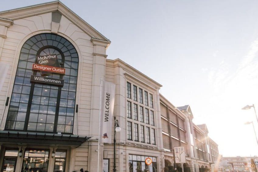 A building with a large arched entrance, a welcome sign, and a designer outlet sign. 2